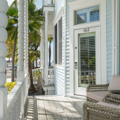 Wicker chairs with striped cushions sit on a porch beside a door numbered