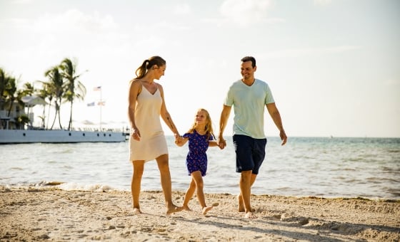 Family walking along the beach, as parents hold their child's hand.