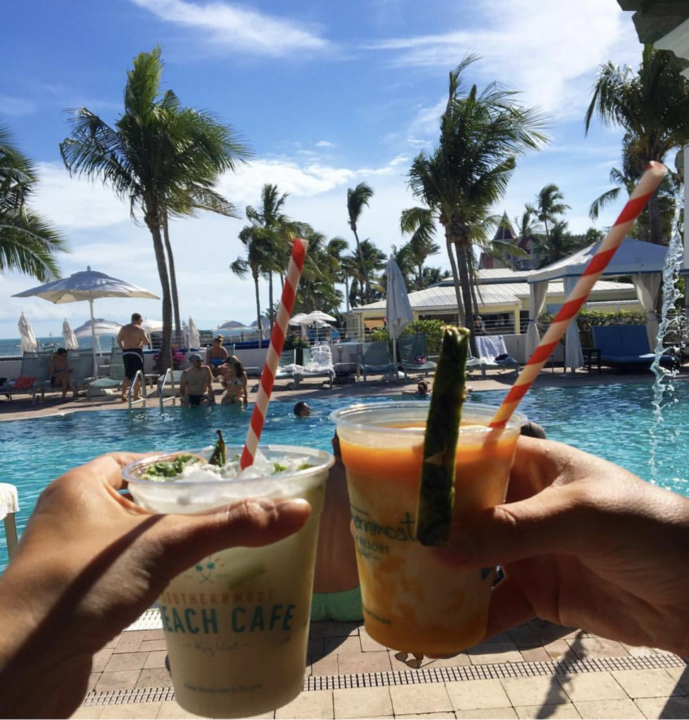 Two cocktails being held beside each other by the pool.