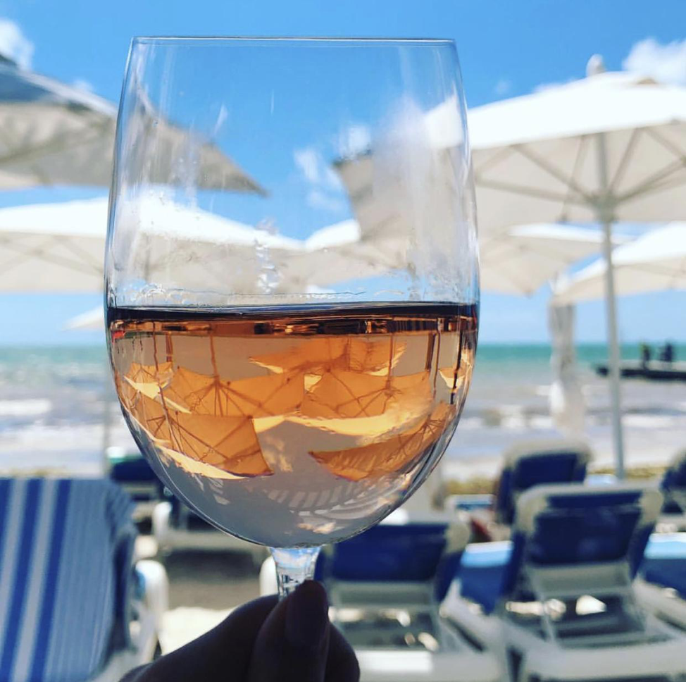 Glass of white wine being held up with white beach umbrellas in the background.