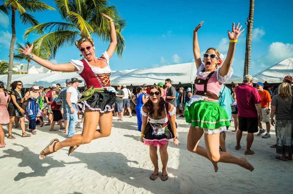 Three women wearing traditional German dirndl dresses and jumping in the air.