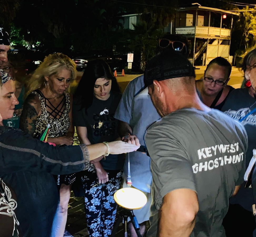 A group of people and their Haunted Key West tour guide joining their right hands in the center of a circle.