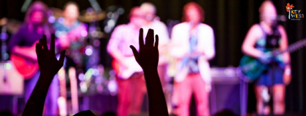 Silhouette of a concert-goers hands amongst a crowd with a band on stage.