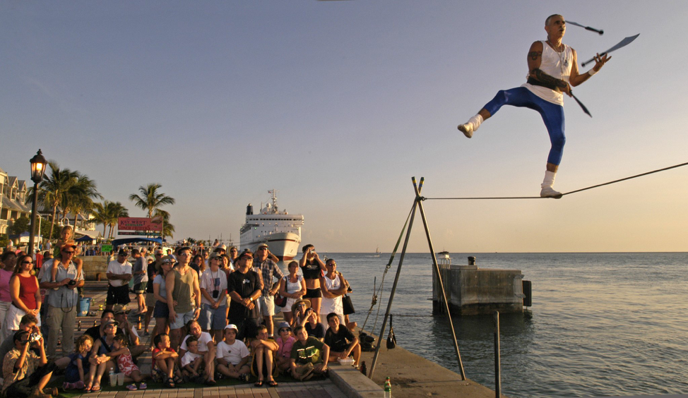 Crowd watches as performer walks along a tight rope, while juggling knives at Mallory Square.