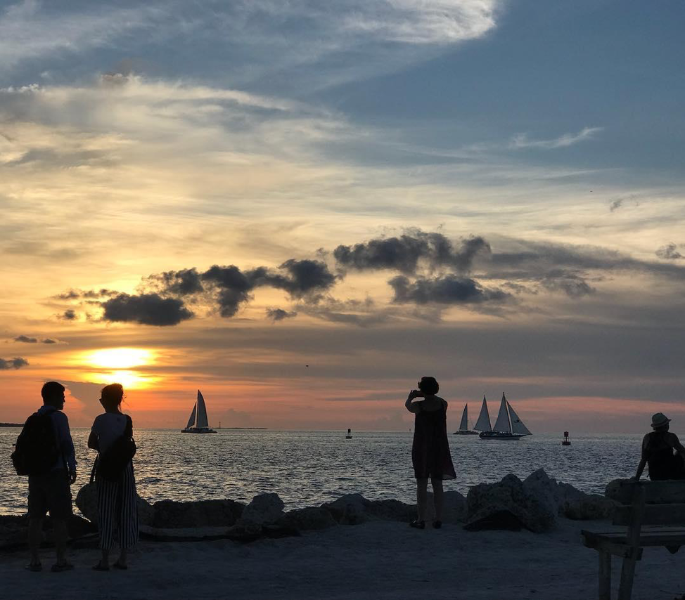 Tourists lounging and taking photos of sailboats and sunset at Fort Zachary Taylor Historic State Park.