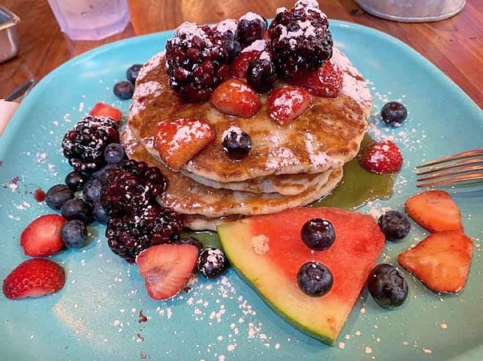 Pancakes with fresh berries and watermelon, sprinkled with icing sugar, and maple syrup