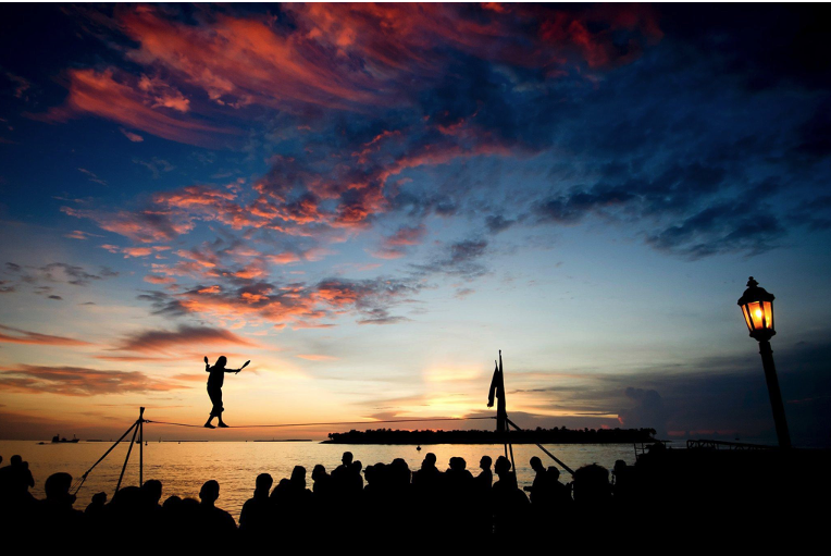 Acrobat walks a tightrope at sunset while crowd watches on