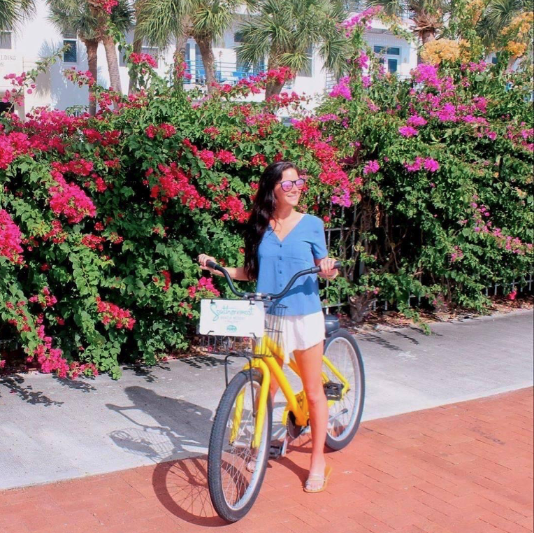 Woman on yellow bike in front of colorful flowers