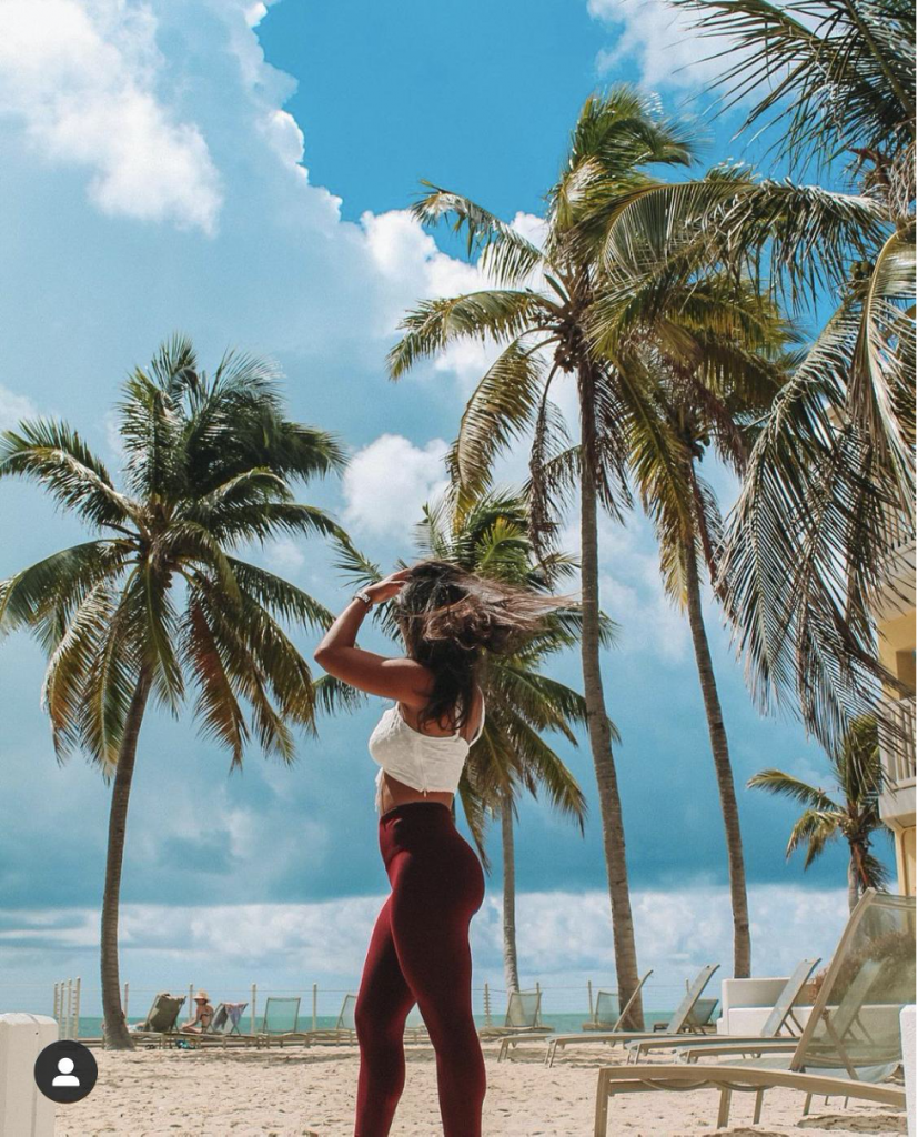 Girl posing with palm trees, clouds, and sandy beach.
