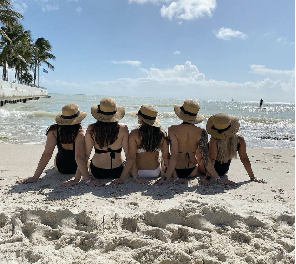 Group of girls sitting on the beach looking at the water. 