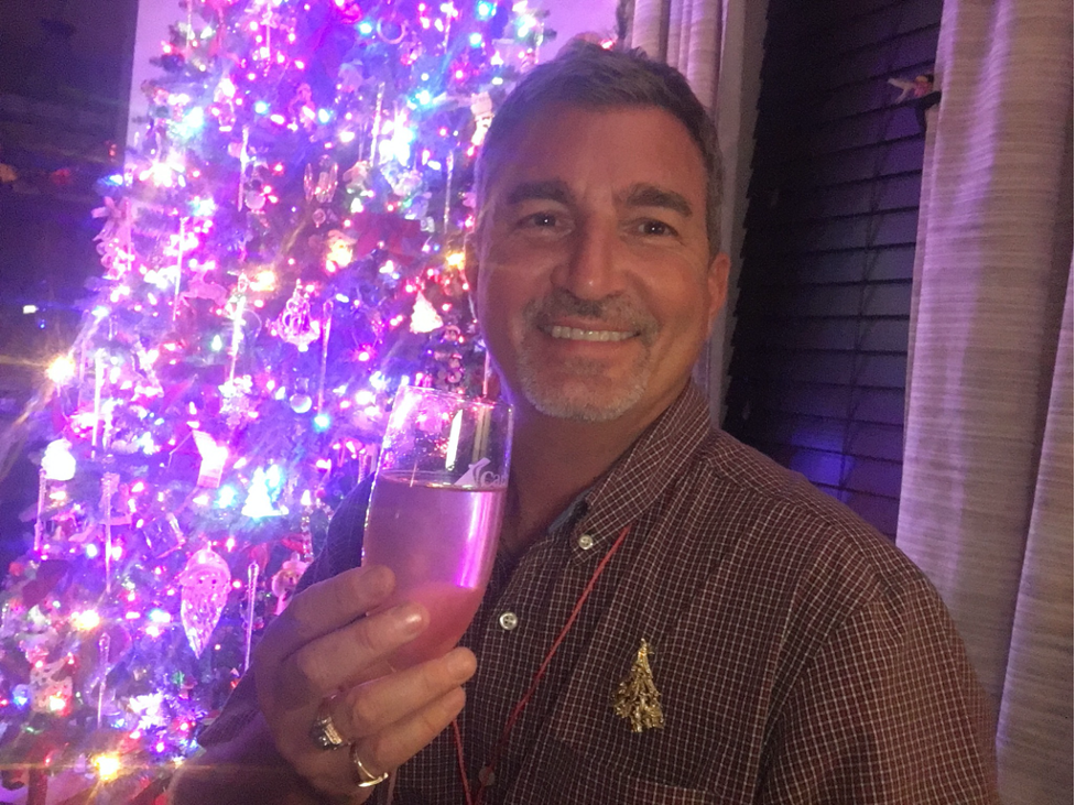 Man holding drink with decorated Christmas tree behind him