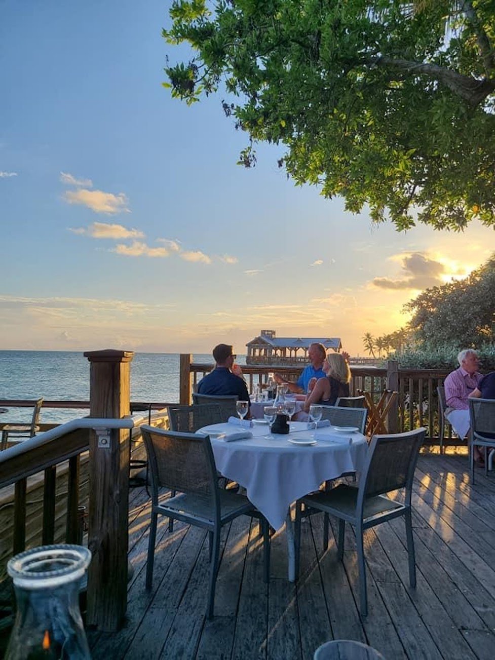 Family enjoying dinner at sunset on a deck overlooking the ocean