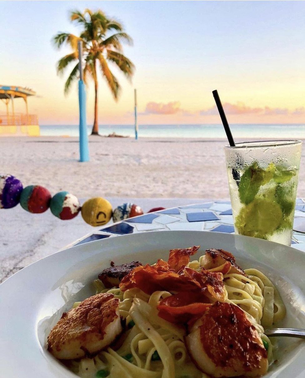 Delicious pasta dish with a tropical view of white sand, palm trees and the ocean.