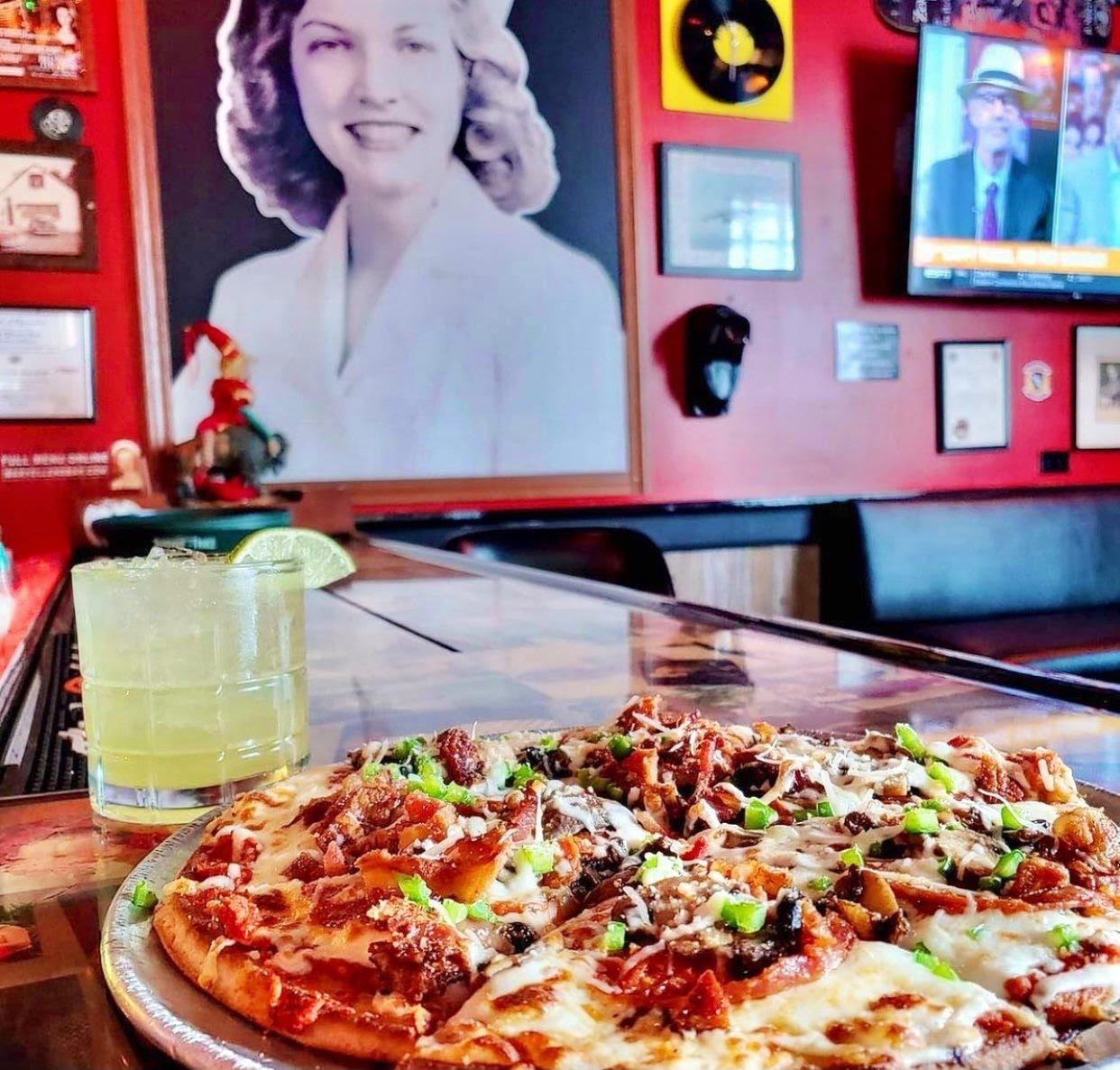 Pizza served with a margarita in restaurant covered in funky artwork