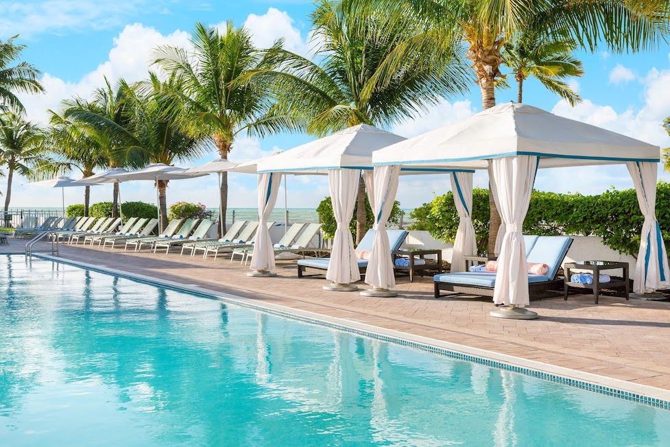 A tropical pool setting surrounded by pool chairs, umbrellas and palm trees