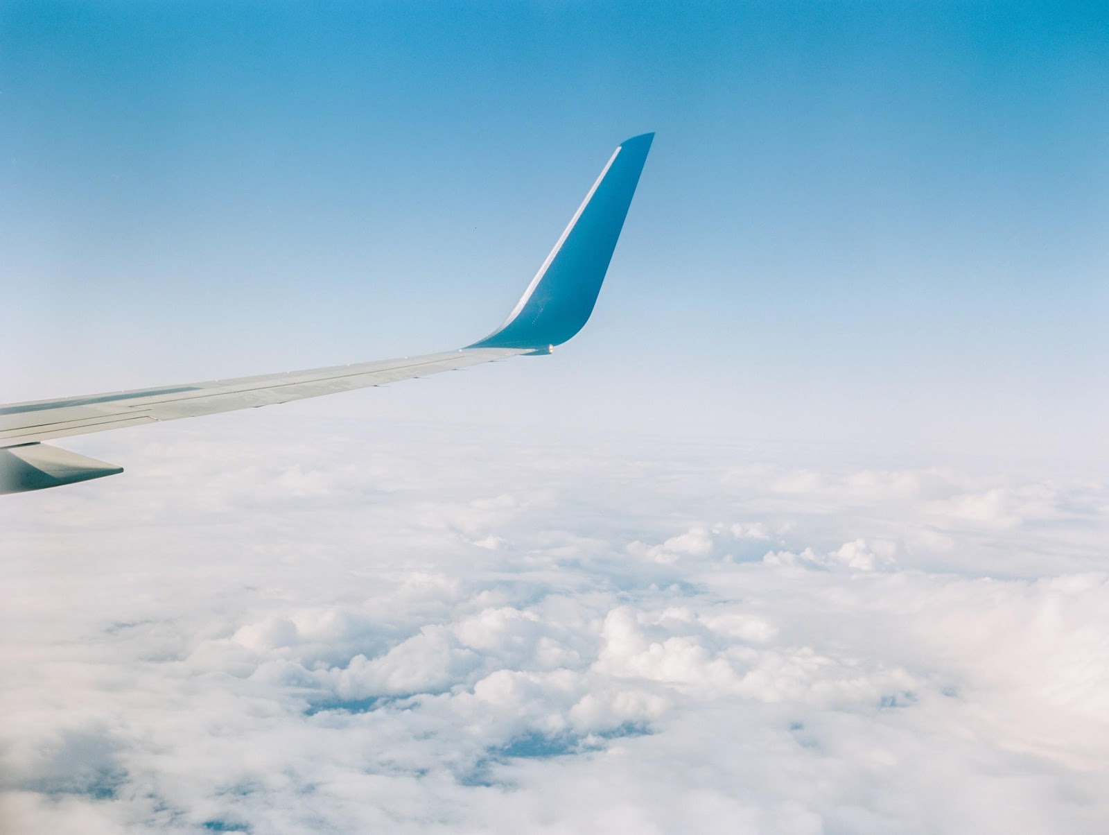 An airplane wing in the clear blue sky surrounded by fluffy white clouds