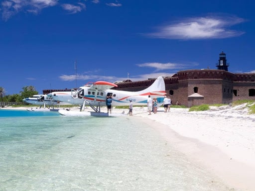 A small airplane on a beach with white sand and clear waters