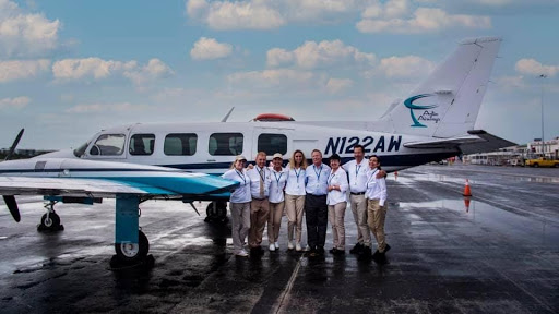 A group of staff posing in front of an airplane on the pavement.