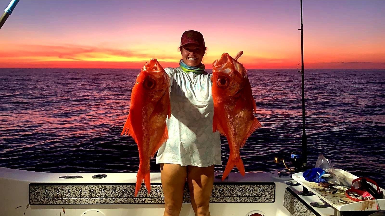 Woman on a boat at sunset with two large fish in her hands