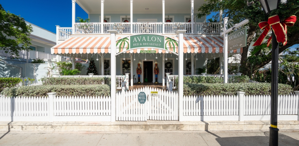 Charming Southernmost Guesthouse Avalon white building with a red awning, nestled behind a pristine white picket fence.