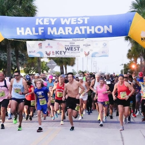 Runners start the marathon under a blue and yellow arch labeled