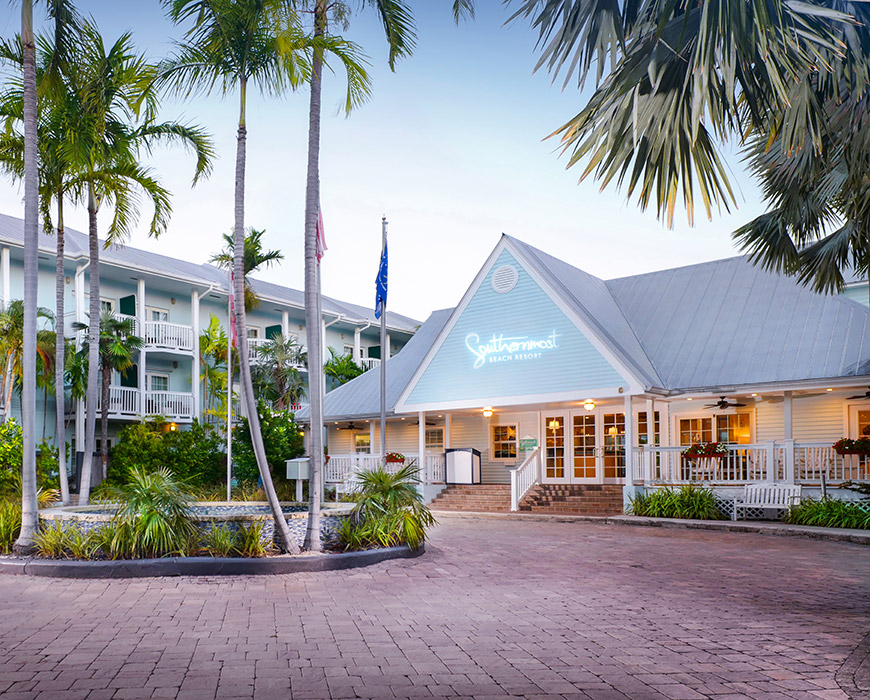 The main building of Southernmost Beach Resort with a large porch and palm trees in front.