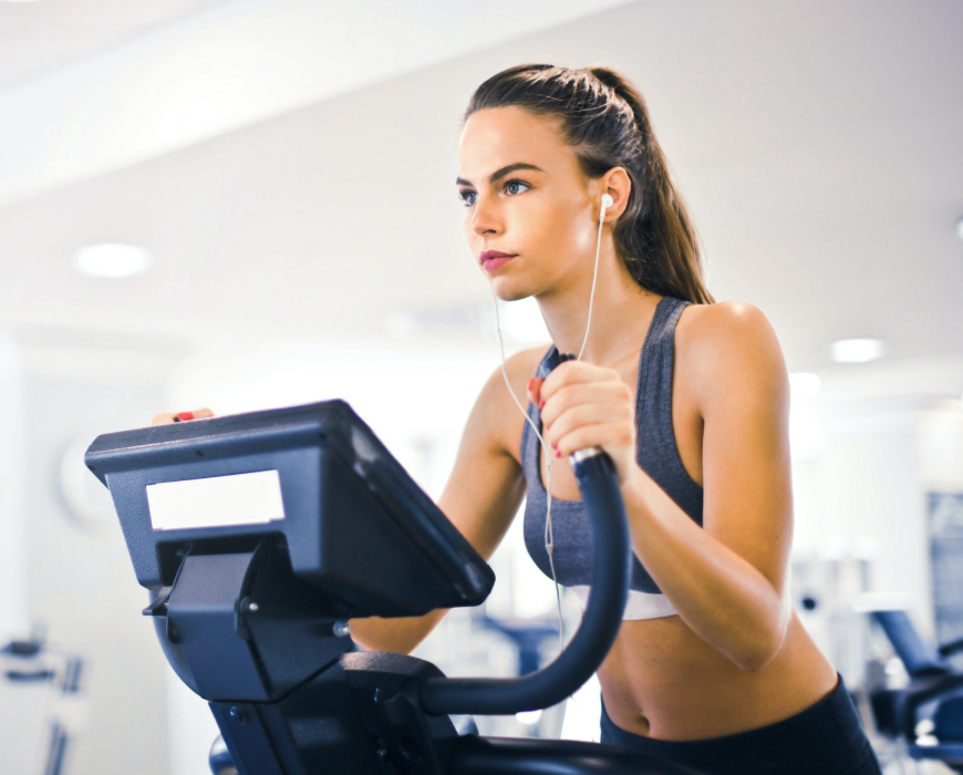a woman in a gray sports bra using a treadmill while wearing earbuds