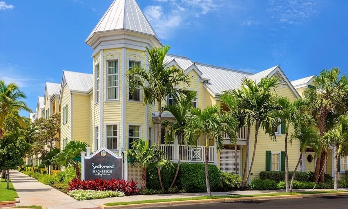 A bright yellow villa surrounded by palm trees on a beautiful day with blue skies