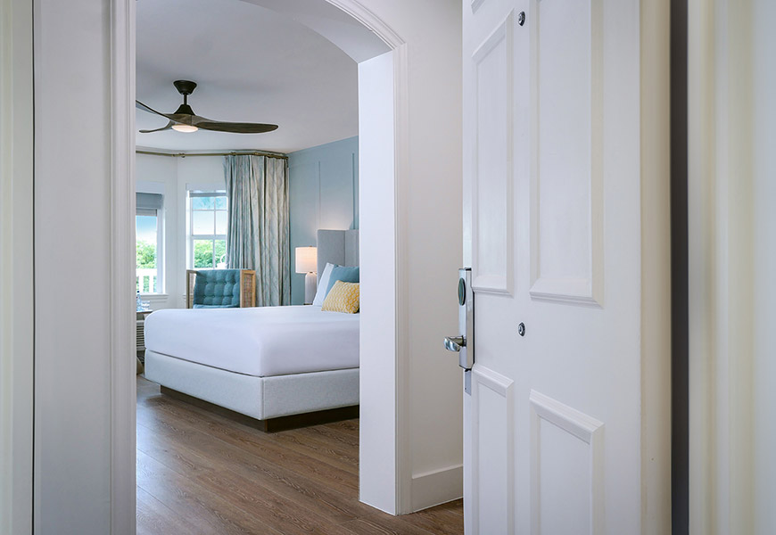 A hotel room with a king-sized bed, seen through an open doorway.
