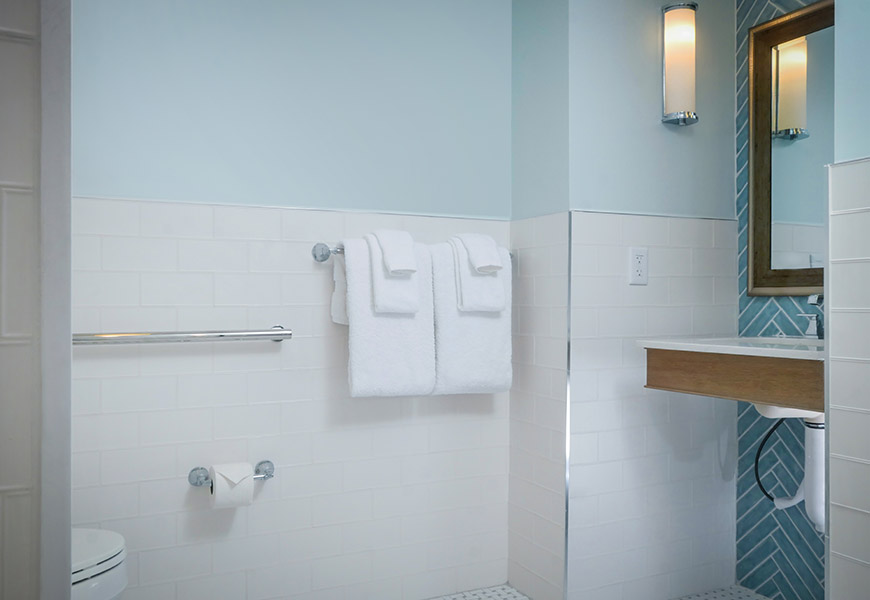 A clean bathroom with white tiled walls, a toilet, sink, and towels.