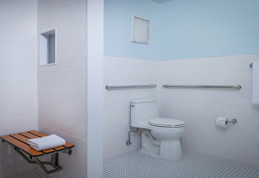 A clean and well-appointed accessible bathroom with a toilet, grab bars, and a fold-down shower seat.