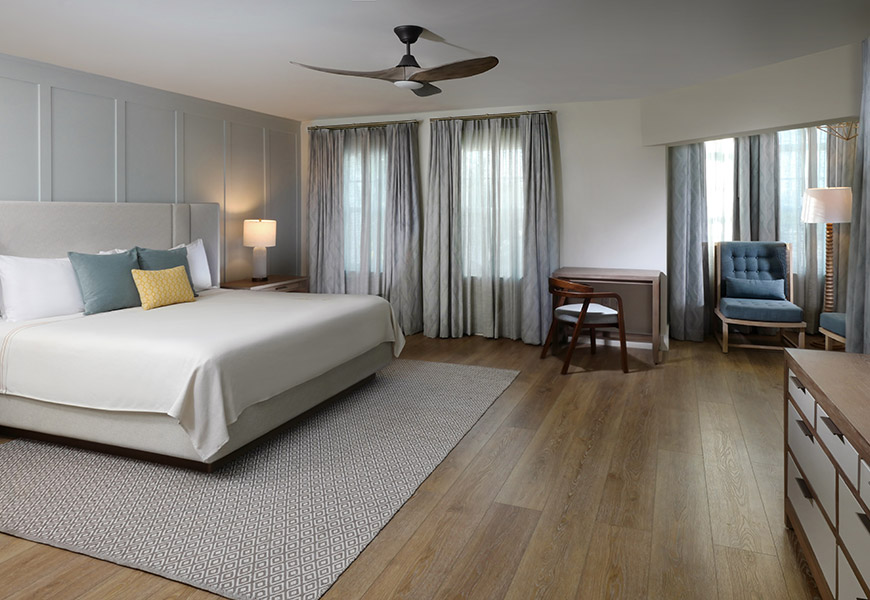 A large hotel room with a bed, desk, chair, and window