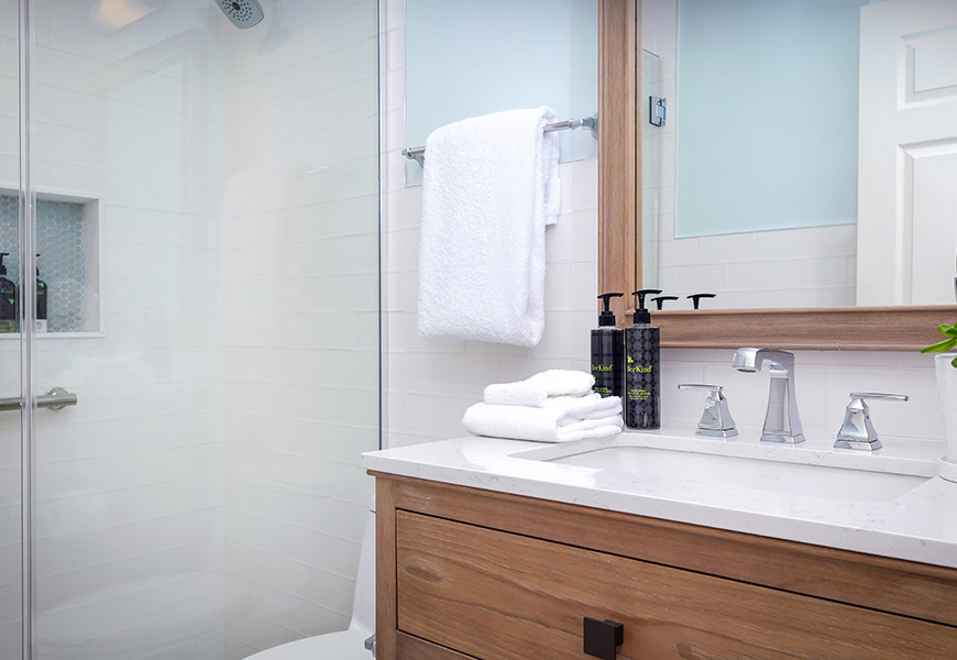 A modern bathroom with a glass-enclosed shower, a wooden cabinet with a marble sink, and white towels.