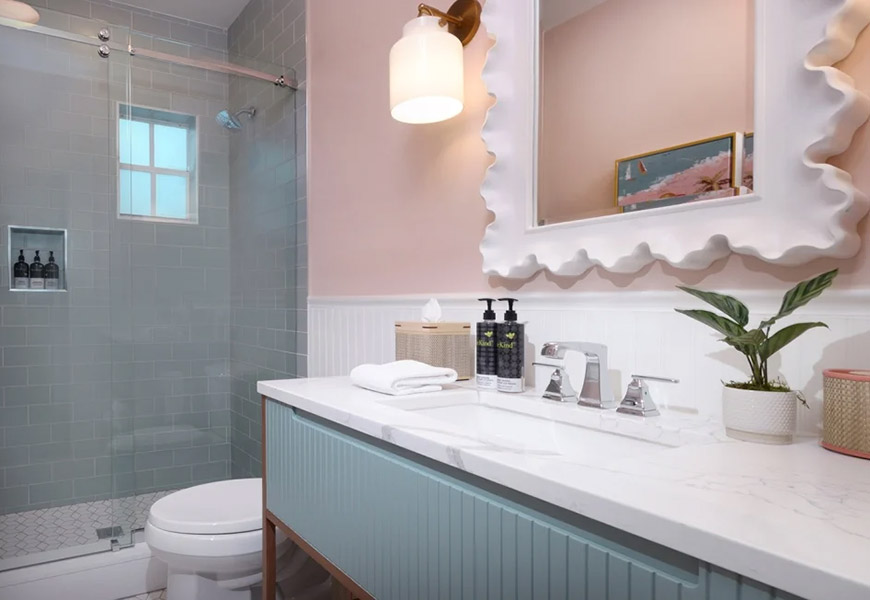 A clean and stylish bathroom with a marble countertop, blue cabinets, and pink walls.