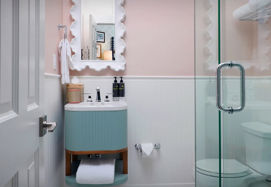 A bathroom with a blue vanity, pink walls, and a glass shower door.