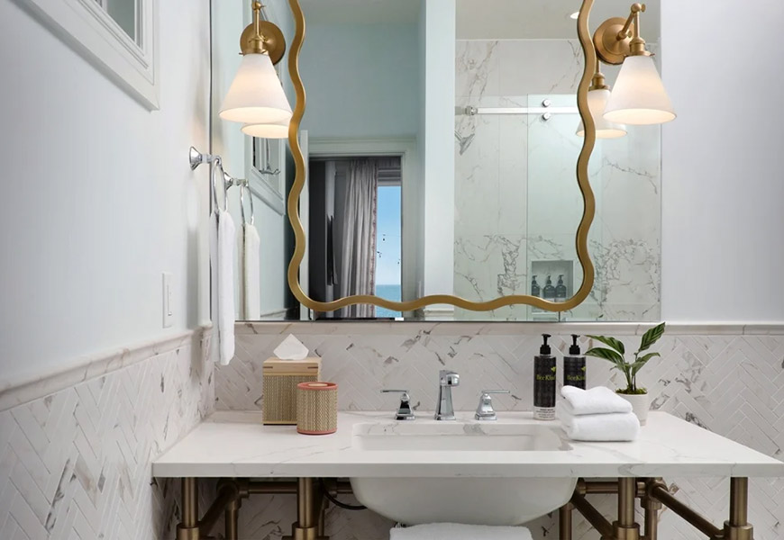 A bathroom vanity with a marble countertop, gold fixtures, and a large mirror