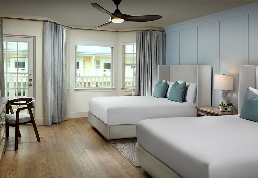 A hotel room with two queen beds, a balcony, and a ceiling fan.