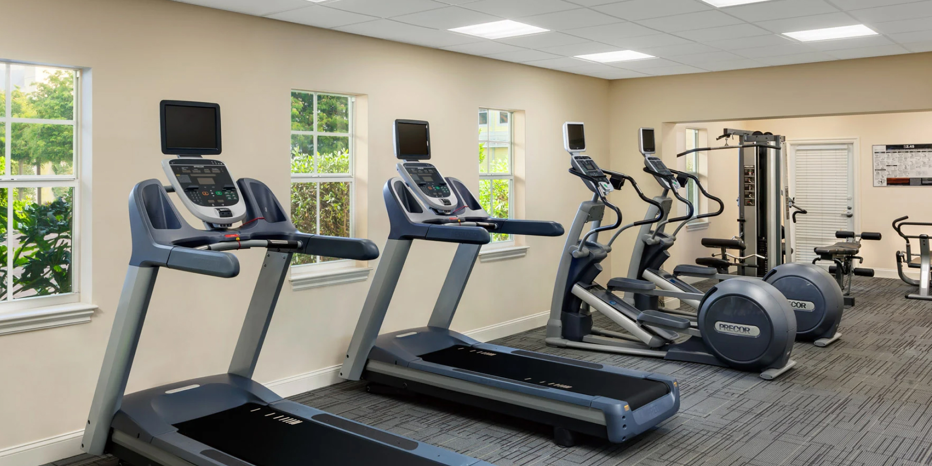 A well-equipped gym with treadmills, elliptical machines, exercise bikes, and weight machines.