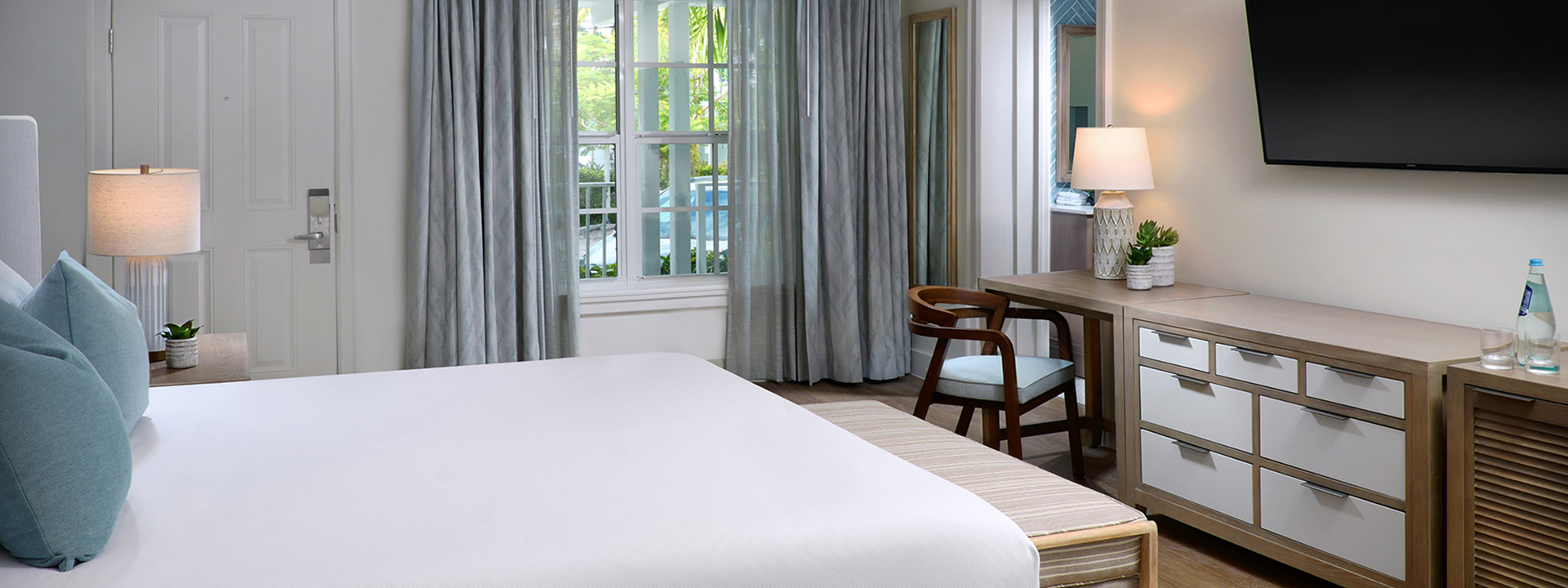 A hotel room with a bed, desk, dresser, and TV