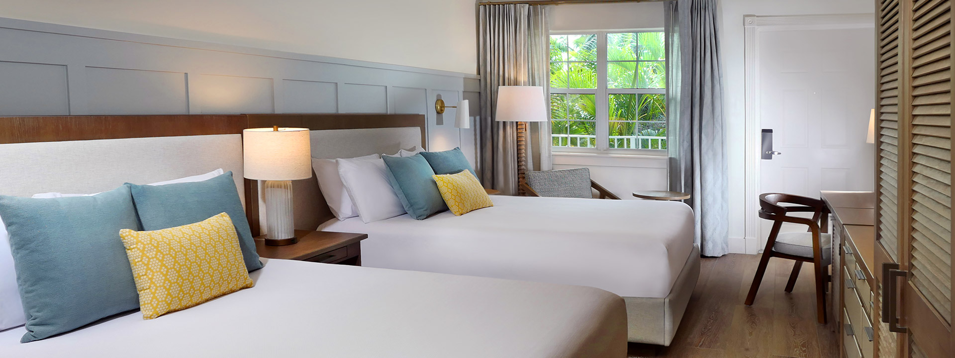 A hotel room with two beds, a window, and a chair