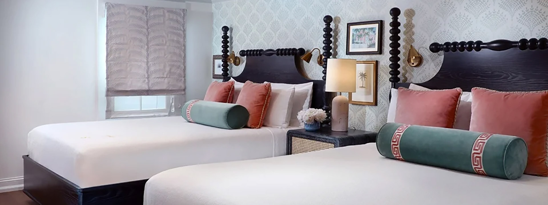 A hotel room with two beds, white comforters, pink pillows, and green bolsters.